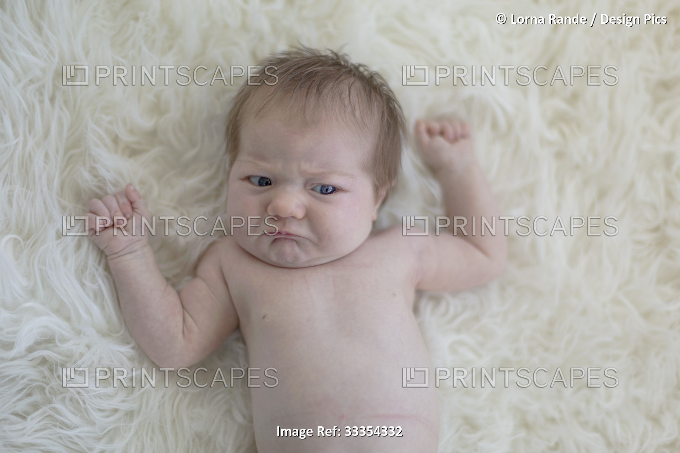 An infant girl lays on a white fur rug making a sad face and about to cry; ...