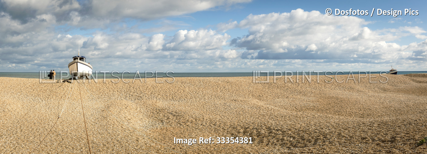 Couple stands at the water's edge looking out into the ocean next to a wooden ...