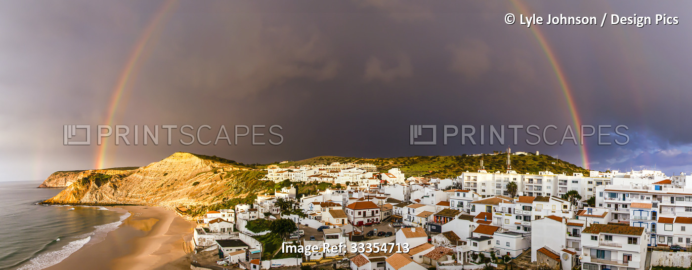 Rainbow arching over the traditional fishing village of Burgau under a stormy ...