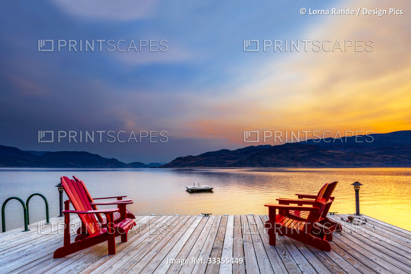 Four red adirondack chairs sit on a large wooden dock on Okanagan Lake at ...