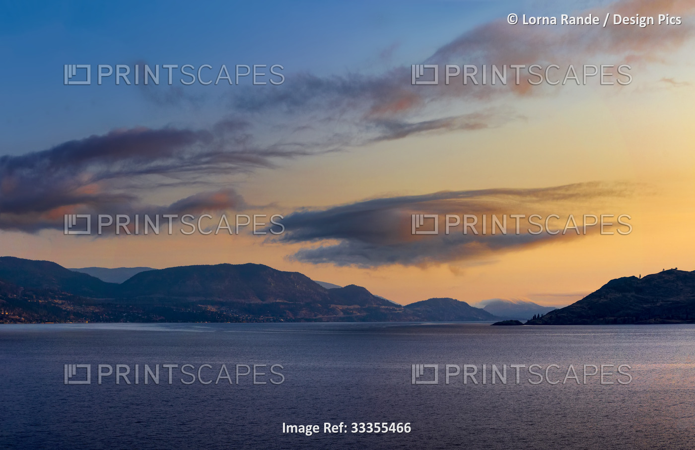 Golden sunset light glowing in the sky over Okanagan Lake and mountain range; ...
