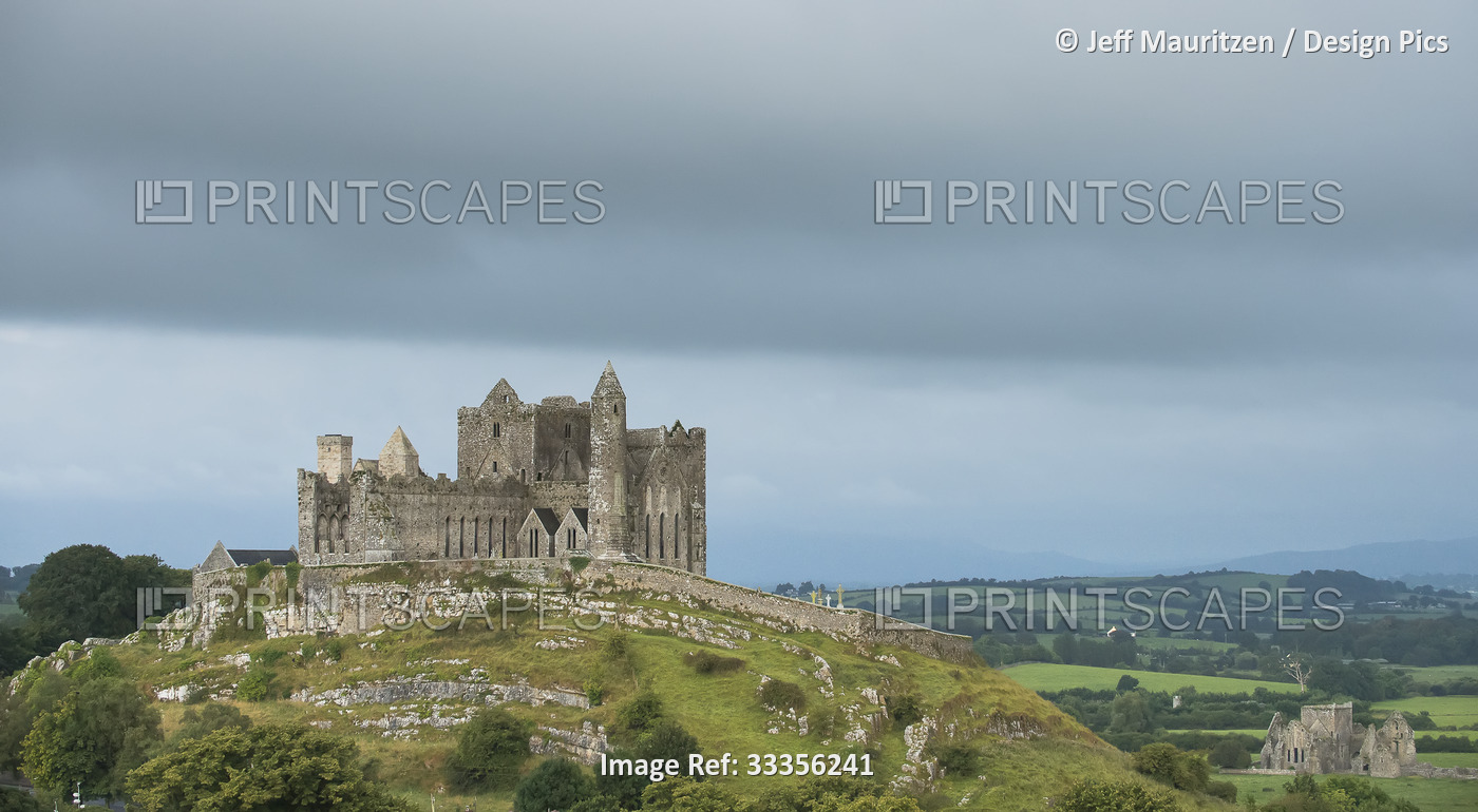 The ancient Rock of Cashel on the hilltop against a cloudy sky with Hore Abbey ...