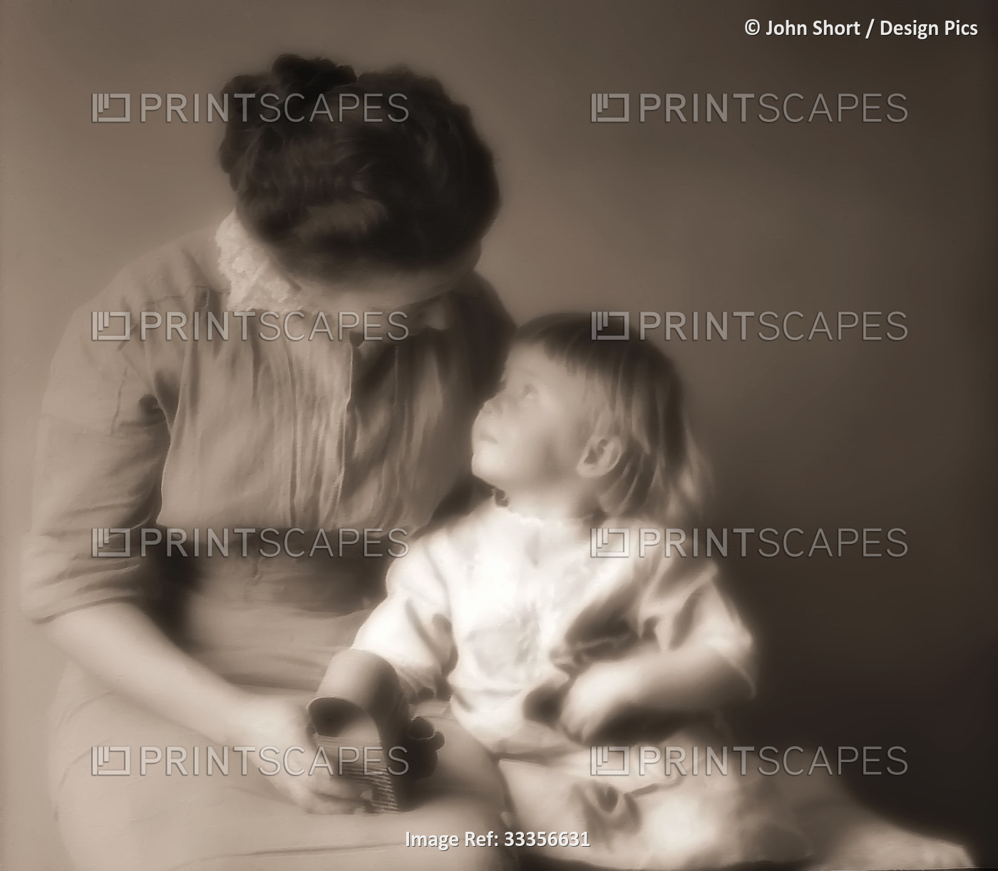Mother sits with her toddler daughter and a holds a toy as they look at each ...
