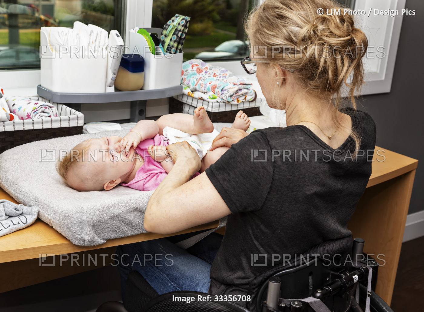 A mother in a wheelchair changes her baby's diaper on a changing table in a ...