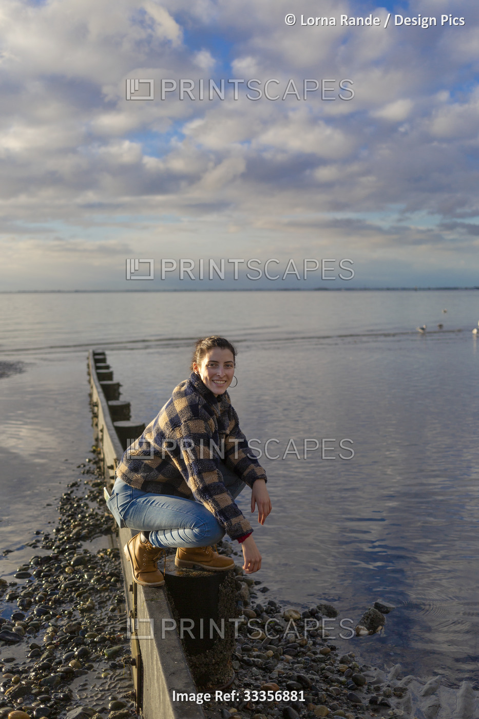 A young woman crouches on a narrow beam on Crescent Beach along the coast of ...
