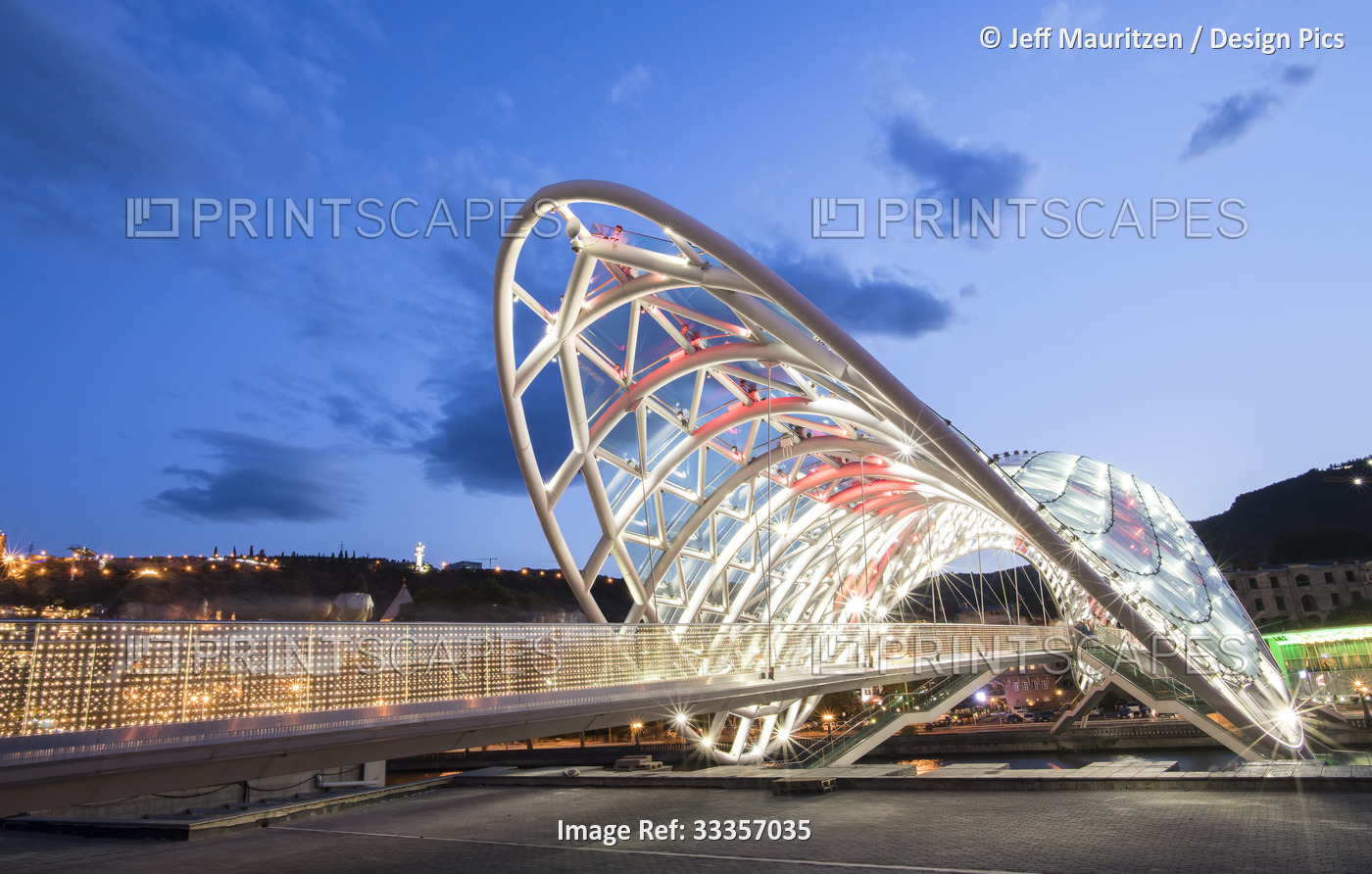 The bow-shaped Bridge of Peace pedestrian bridge, illuminated at dusk spanning ...