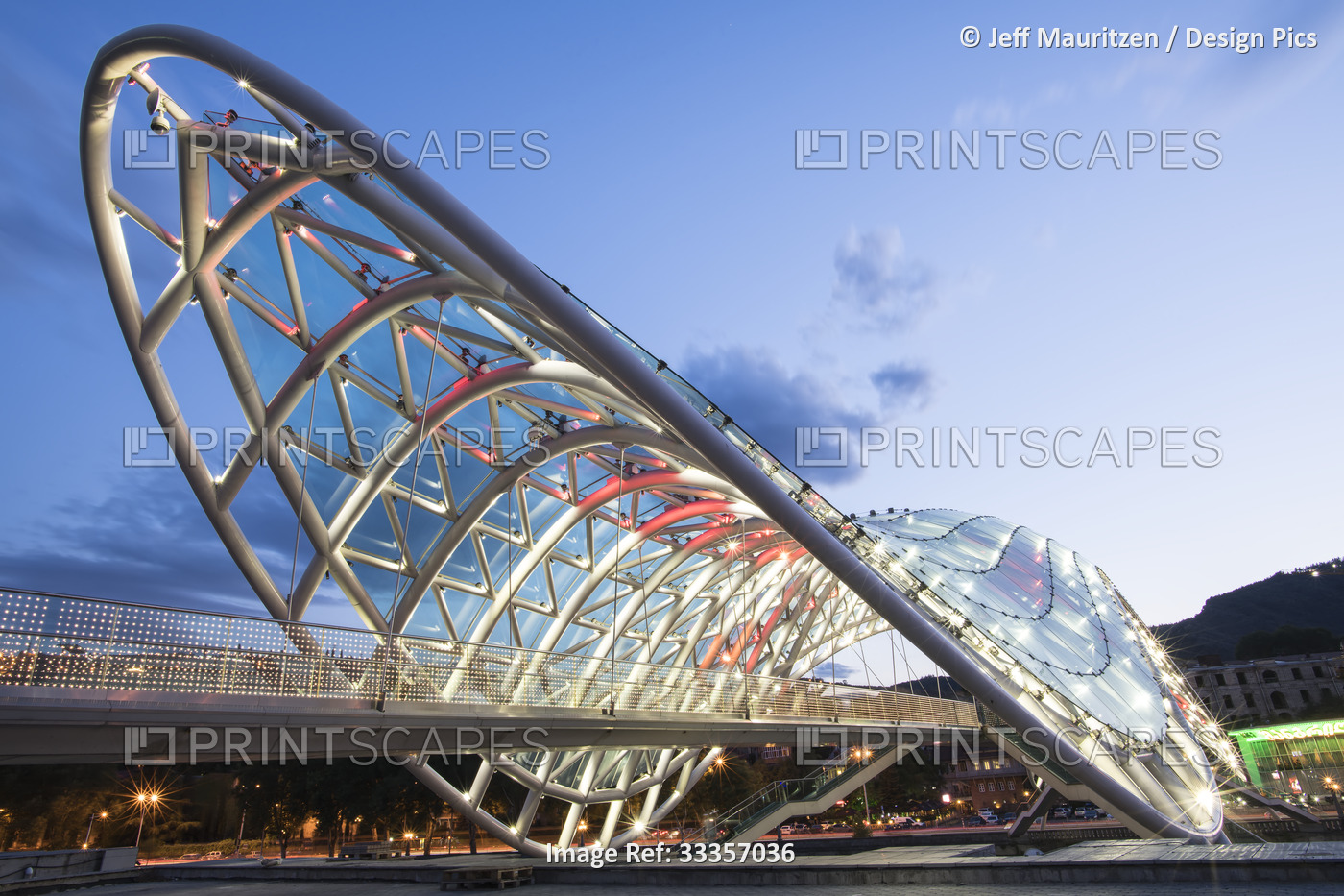 The bow-shaped Bridge of Peace pedestrian bridge, illuminated at dusk spanning ...