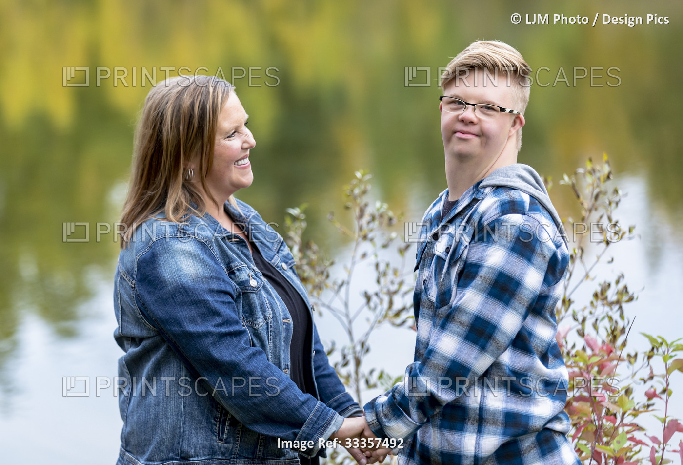 A young man with Down Syndrome holding hands with his mother and looking at the ...