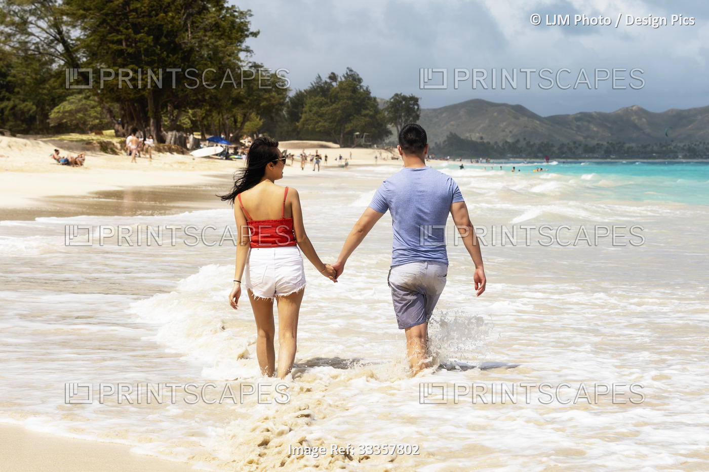 A couple walks down a white sand beach holding hands while enjoying a tropical ...