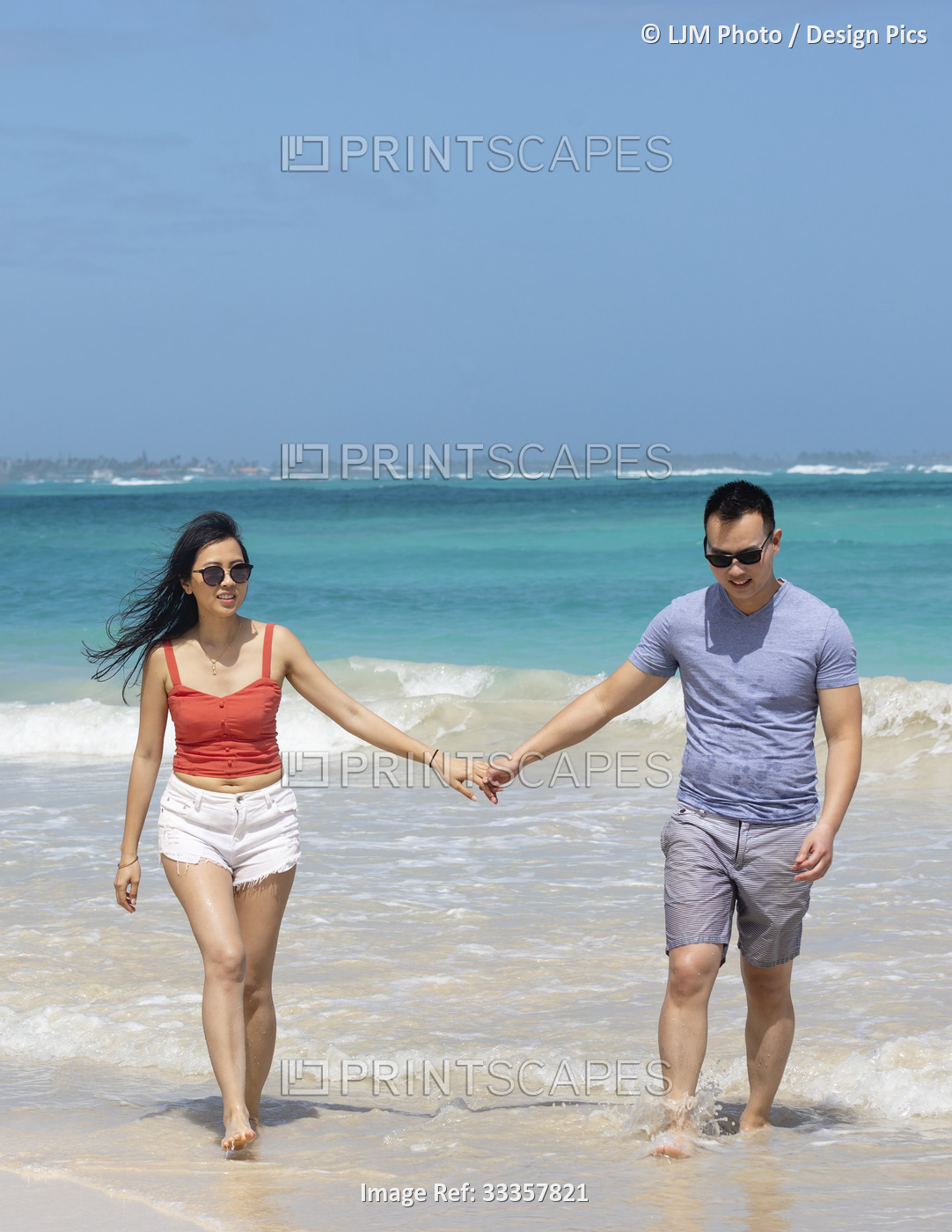 A couple walks down a white sand beach holding hands while enjoying a tropical ...