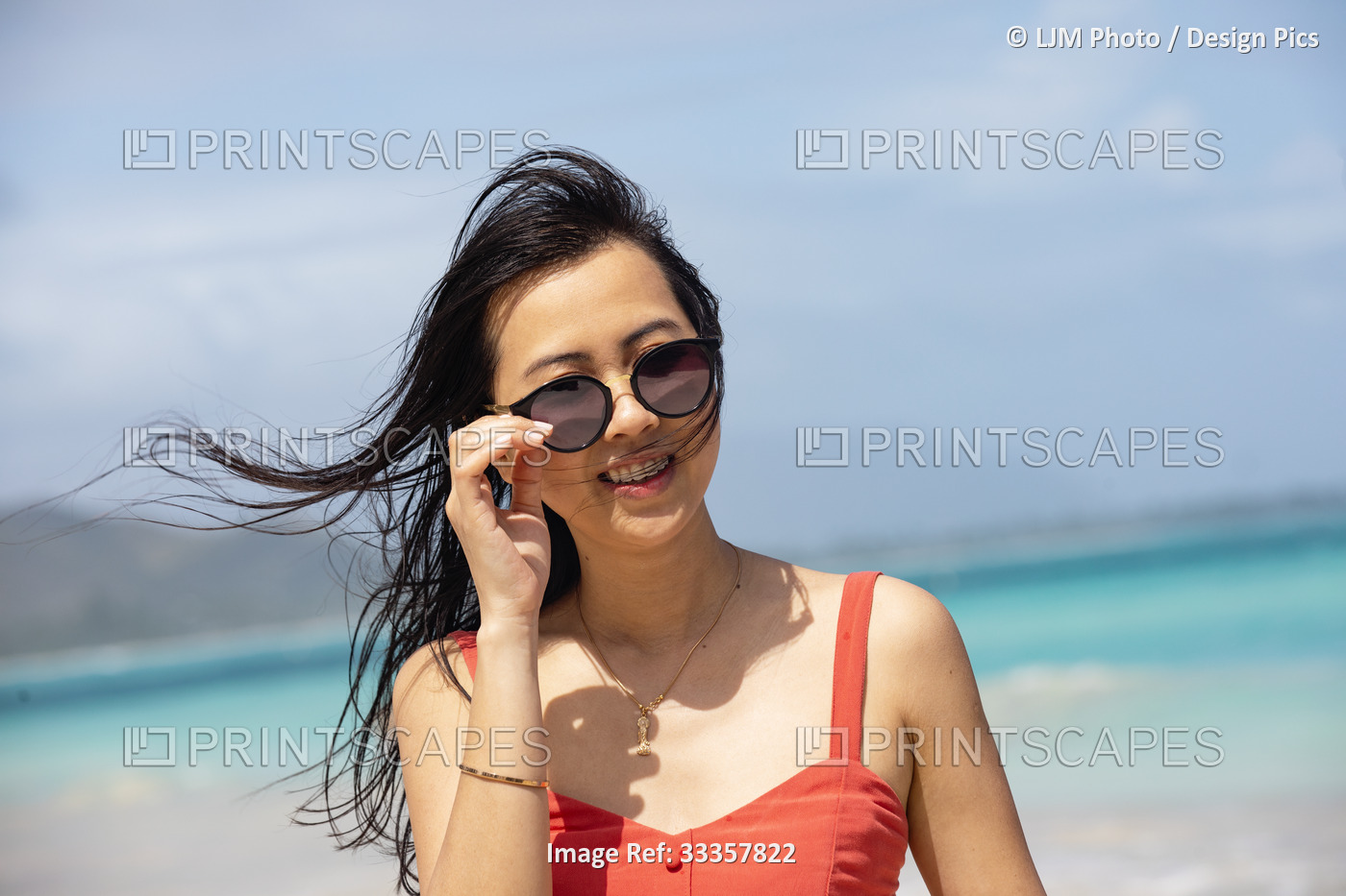 Portrait of an Asian woman with sunglasses standing along the coast of Oahu ...