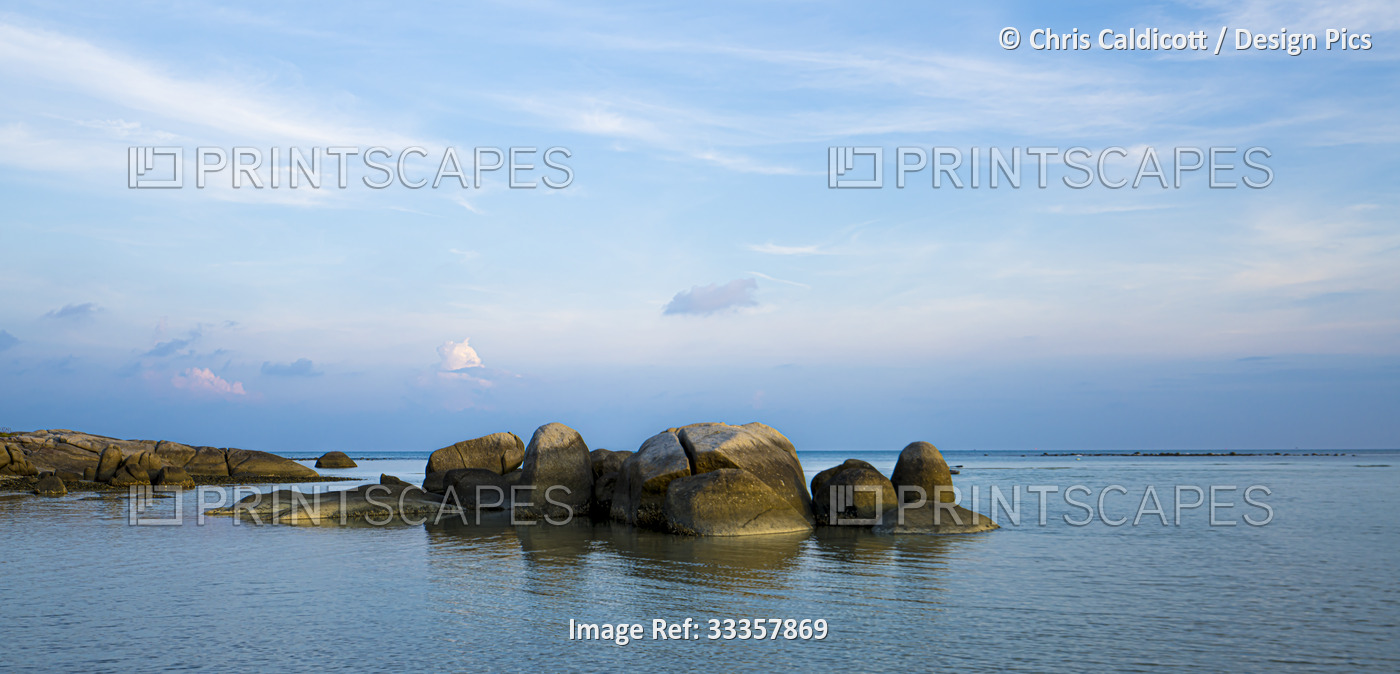 Dawn over a lagoon with rock formations along the shore of the calm, waters on ...