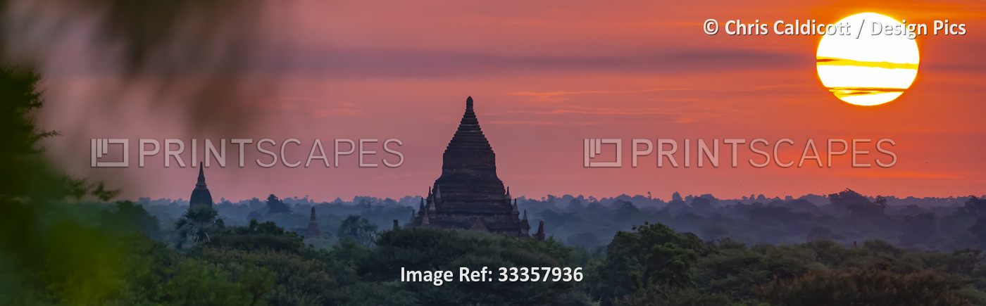 Silhouettes of pagodas with the sun rising above the Plain of Bagan at dawn; ...