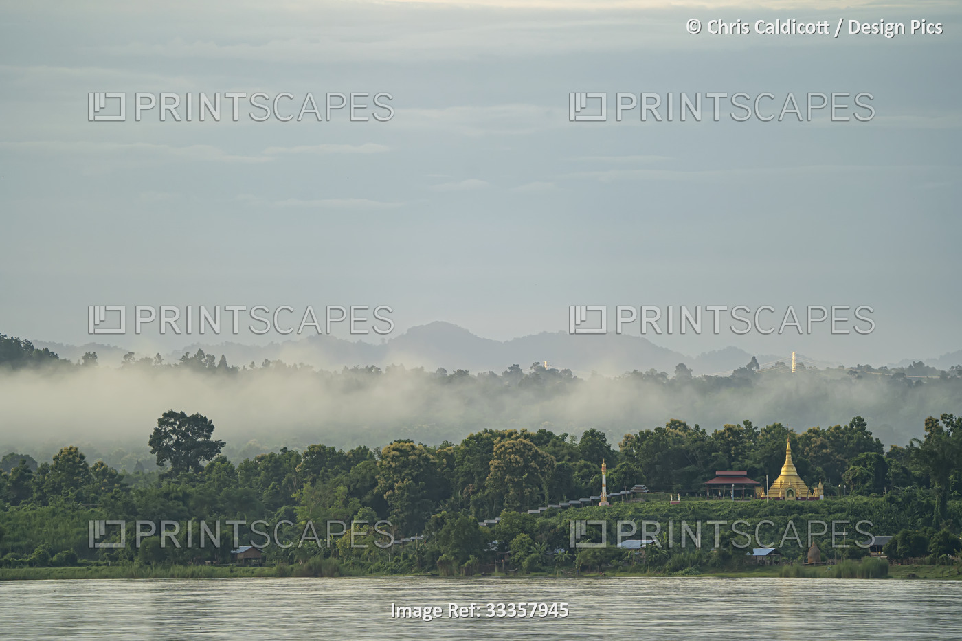 Dawn morning mist rising over a village stupa on the jungle covered banks of ...