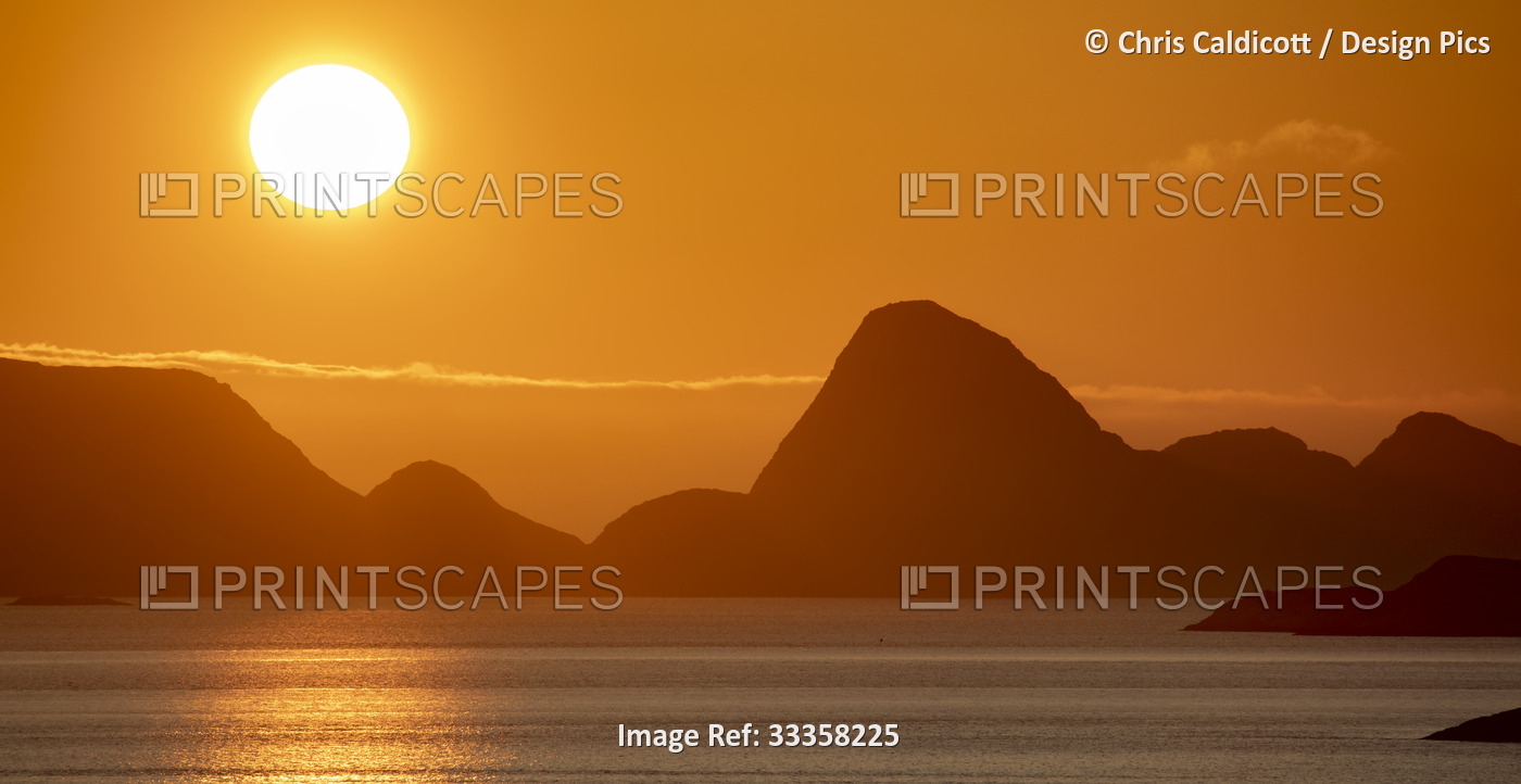 Midnight Sun glowing brightly in the orange sky over the mountain peaks and ...