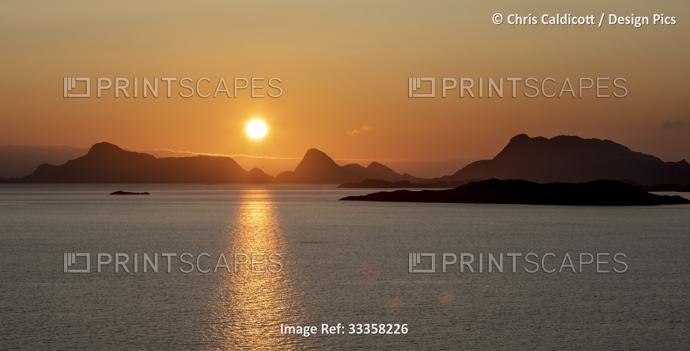 Midnight Sun glowing brightly over the mountain peaks and reflecting on the ...
