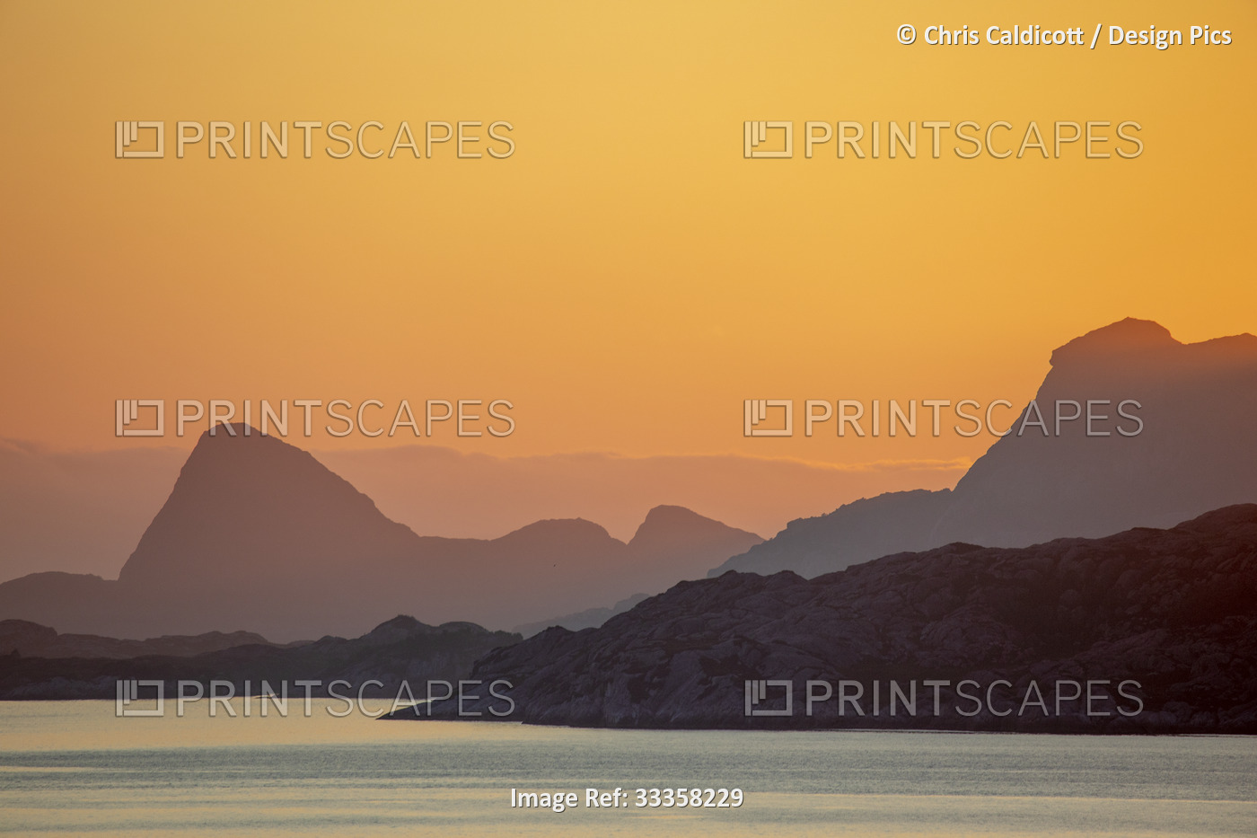 Golden sky of the Midnight Sun glowing from behind the mountain peaks along the ...