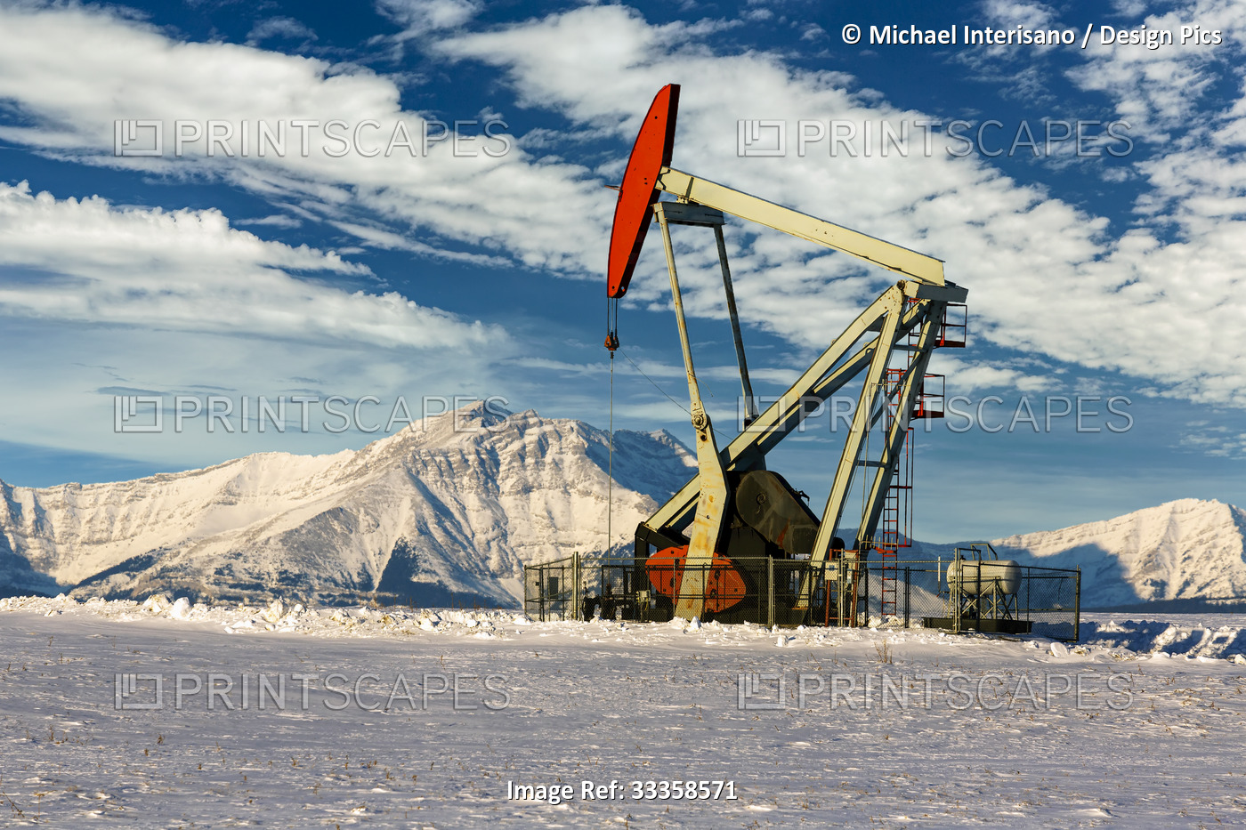 Pumpjack in a snow-covered field with dramatic clouds in a blue sky with ...