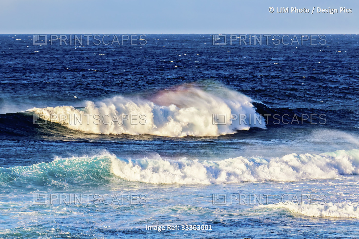 Splashing waves create a rainbow of colour in the mist with a blue seascape and ...