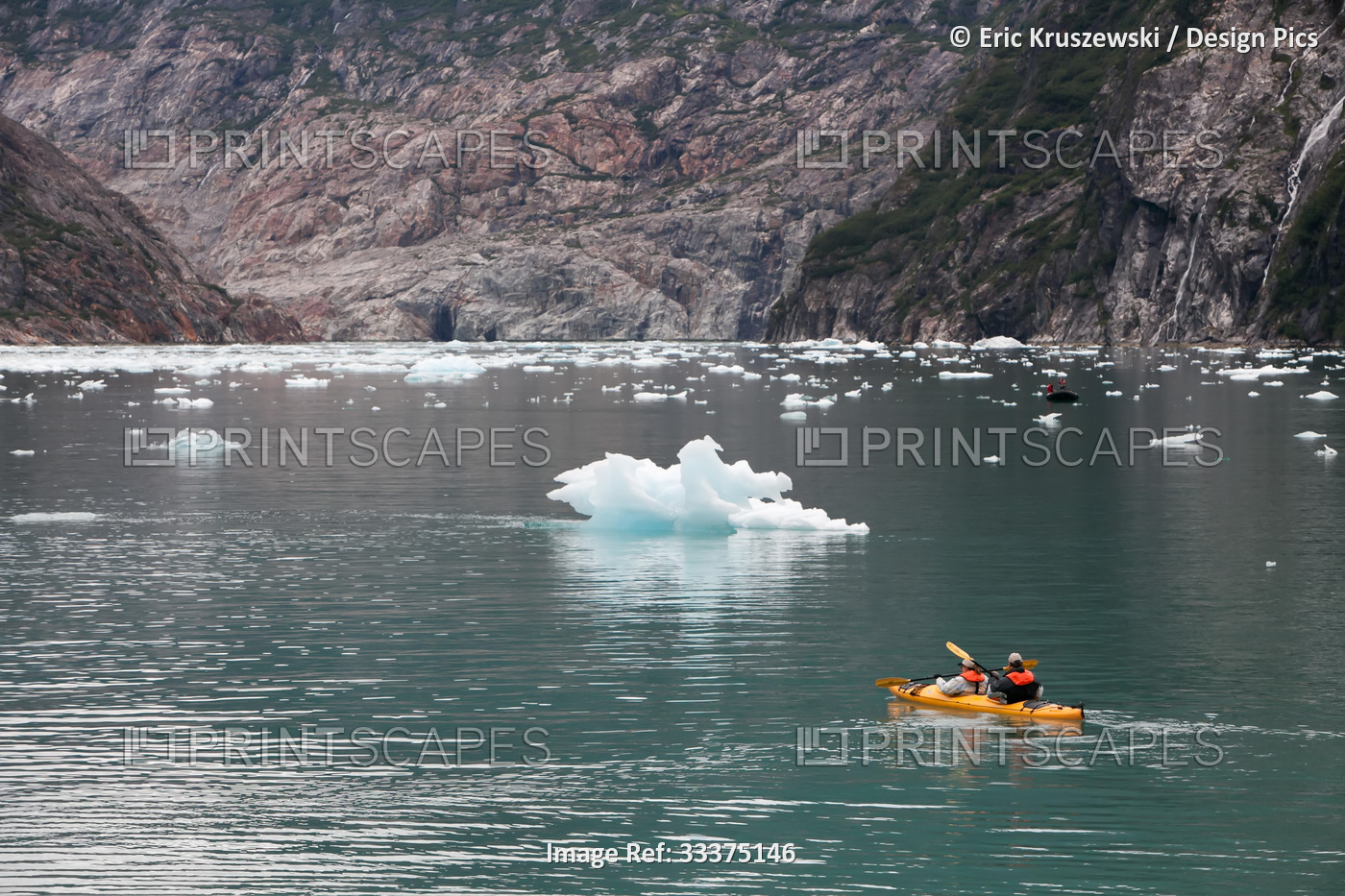 Near dramatic landscape, travelers in a kayak navigate water around icebergs.; ...
