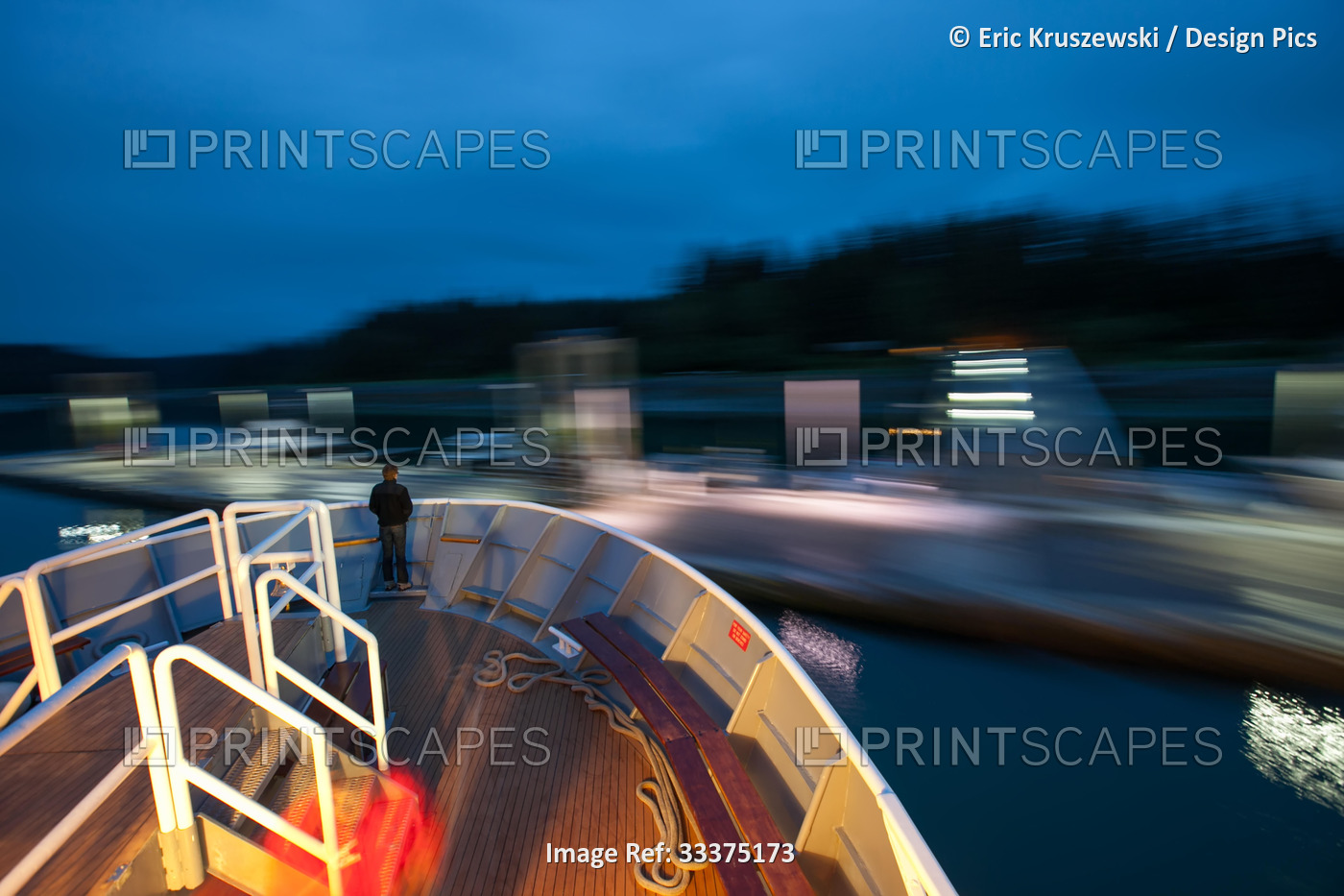 At twilight, a passenger stands on the bow of an expedition cruise ship as it ...
