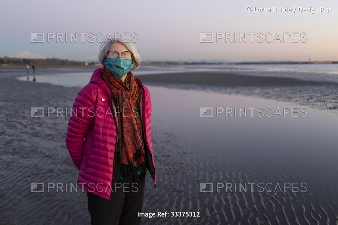 A senior woman stands on a wet beach wearing a face mask during the global ...