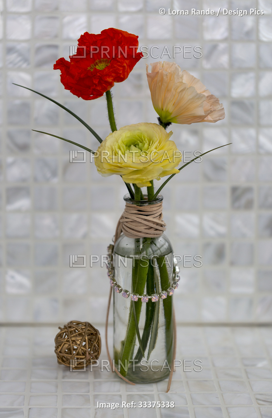 Colorful poppies and ranunculus in a glass vase wrapped with leather cord and a ...