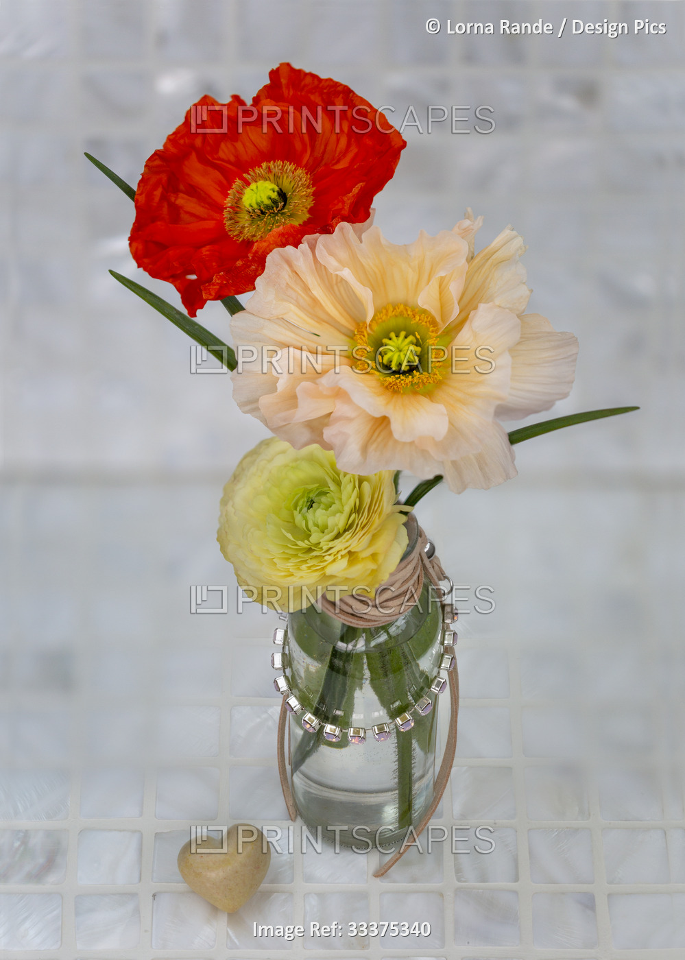 View form above of colorful poppies and ranunculus in a glass vase wrapped with ...