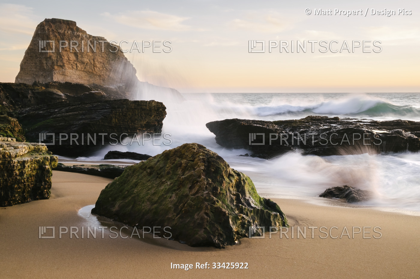 Sunset along the central California coast with waves crashing onto the large ...