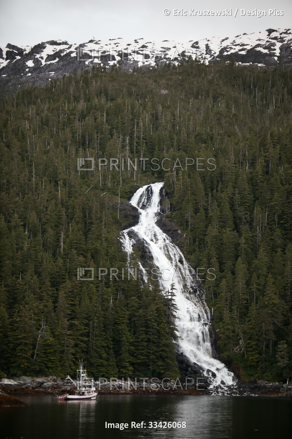 A small boat navigates near a waterfall that was formed from glacier runoff.; ...