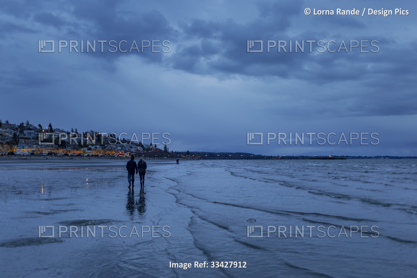 A couple walking on the beach at sunset during low tide in White Rock, BC, ...