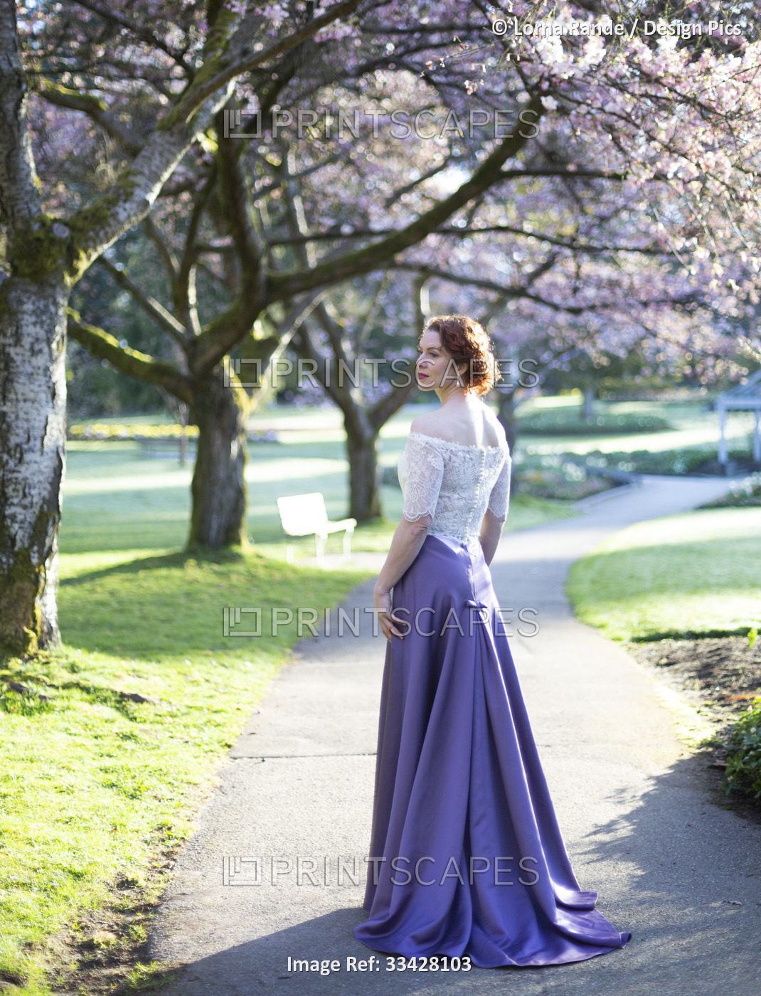 A woman with red curly hair and formal gown standing on a footpath in the ...