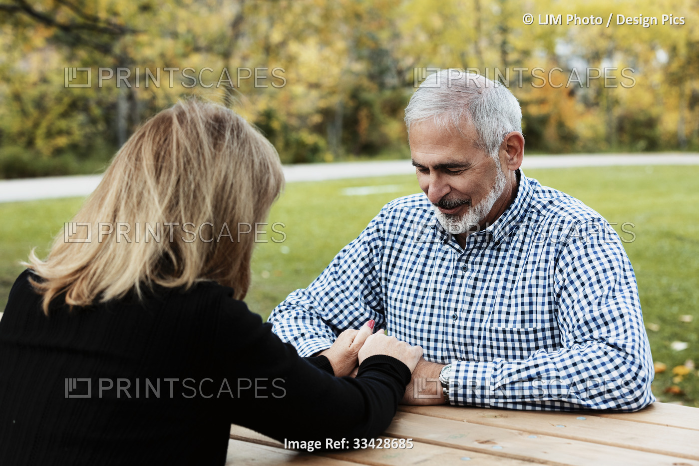 A mature couple praying together at a picnic table on a warm fall day in a city ...