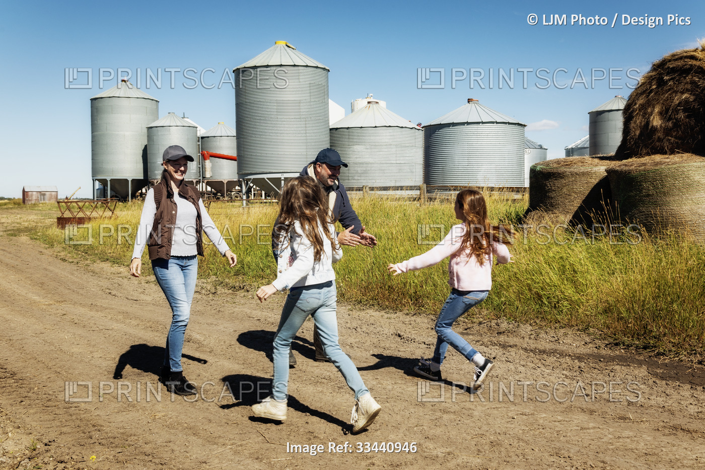 Two young girls running to greet their parents on their family farm with grain ...