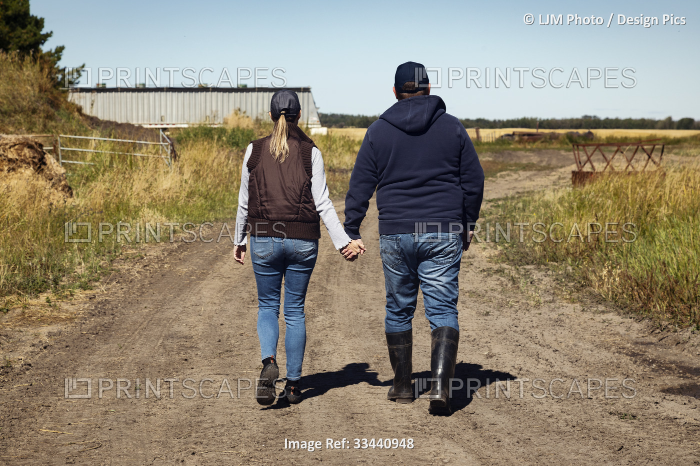 View Taken from behind of a mature couple holding hands and walking along a ...