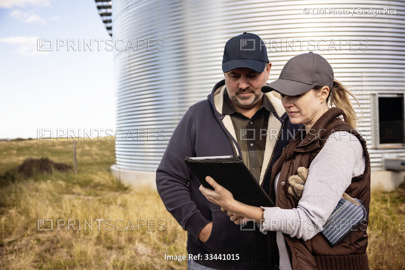 Mature couple working on their farm, standing in front of grain bins consulting ...