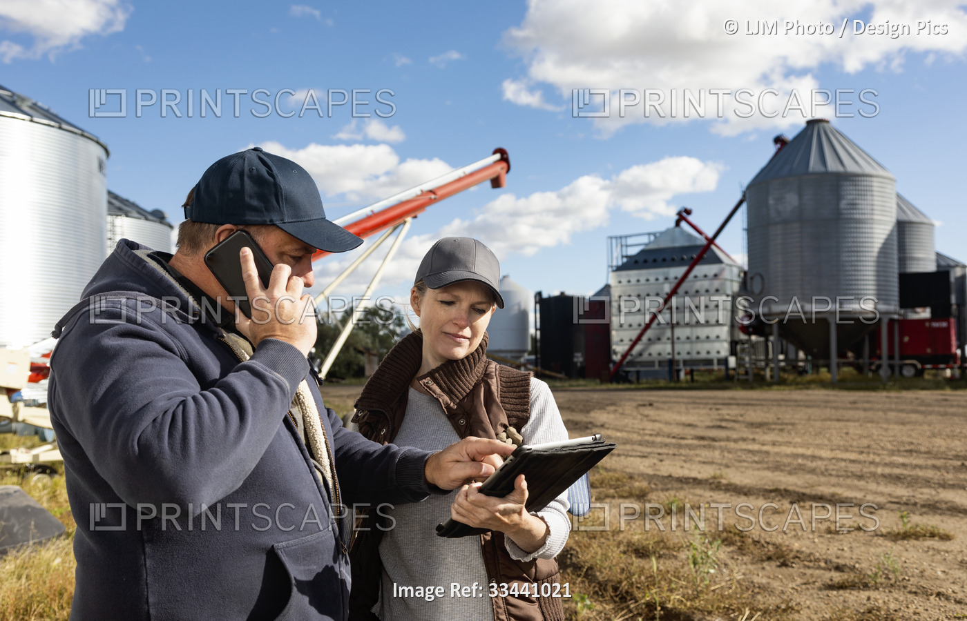 Mature couple working on their farm, standing in front of their grainery while ...
