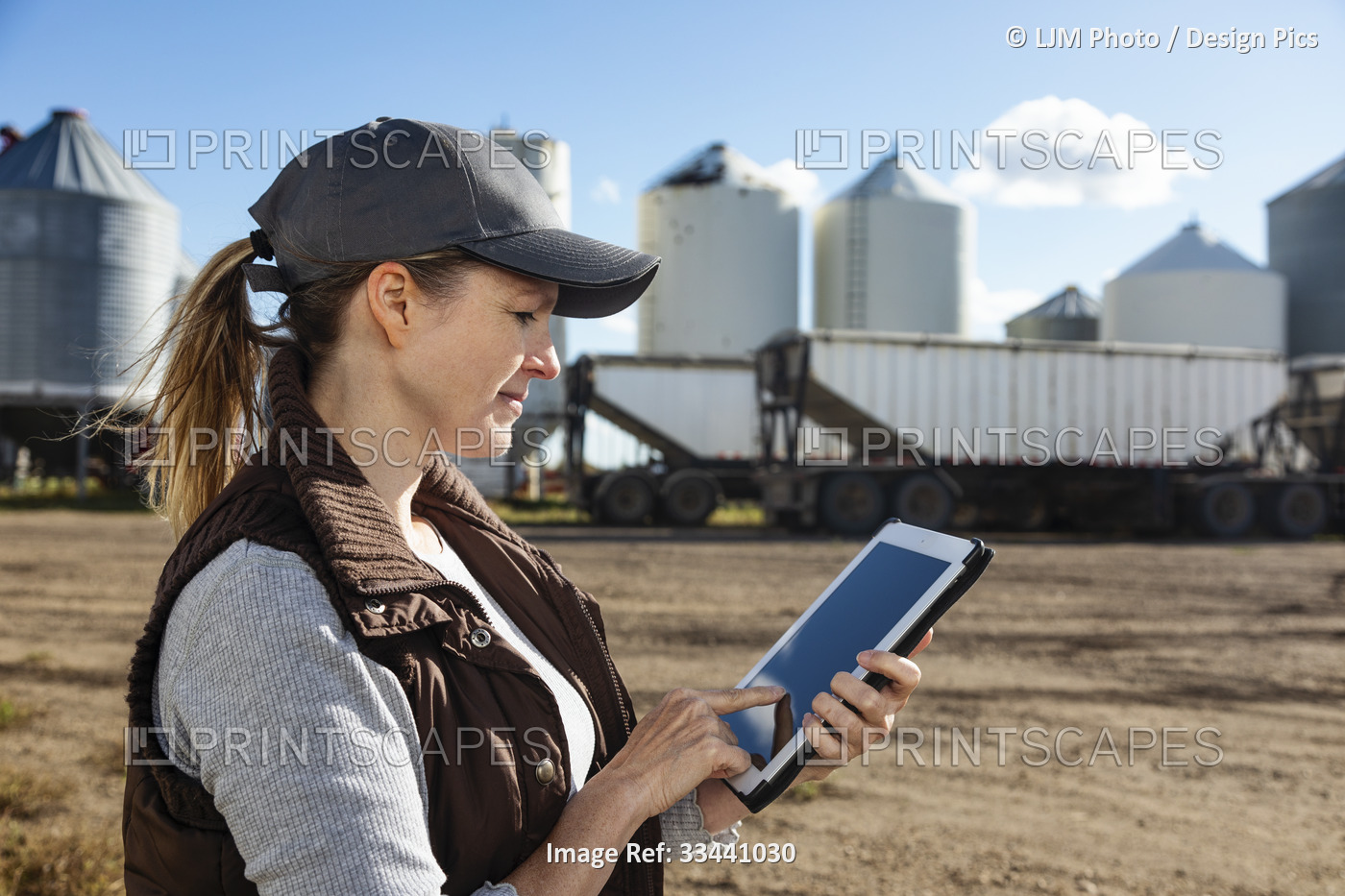 Mature woman farmer working on a tablet computer and standing in front of grain ...
