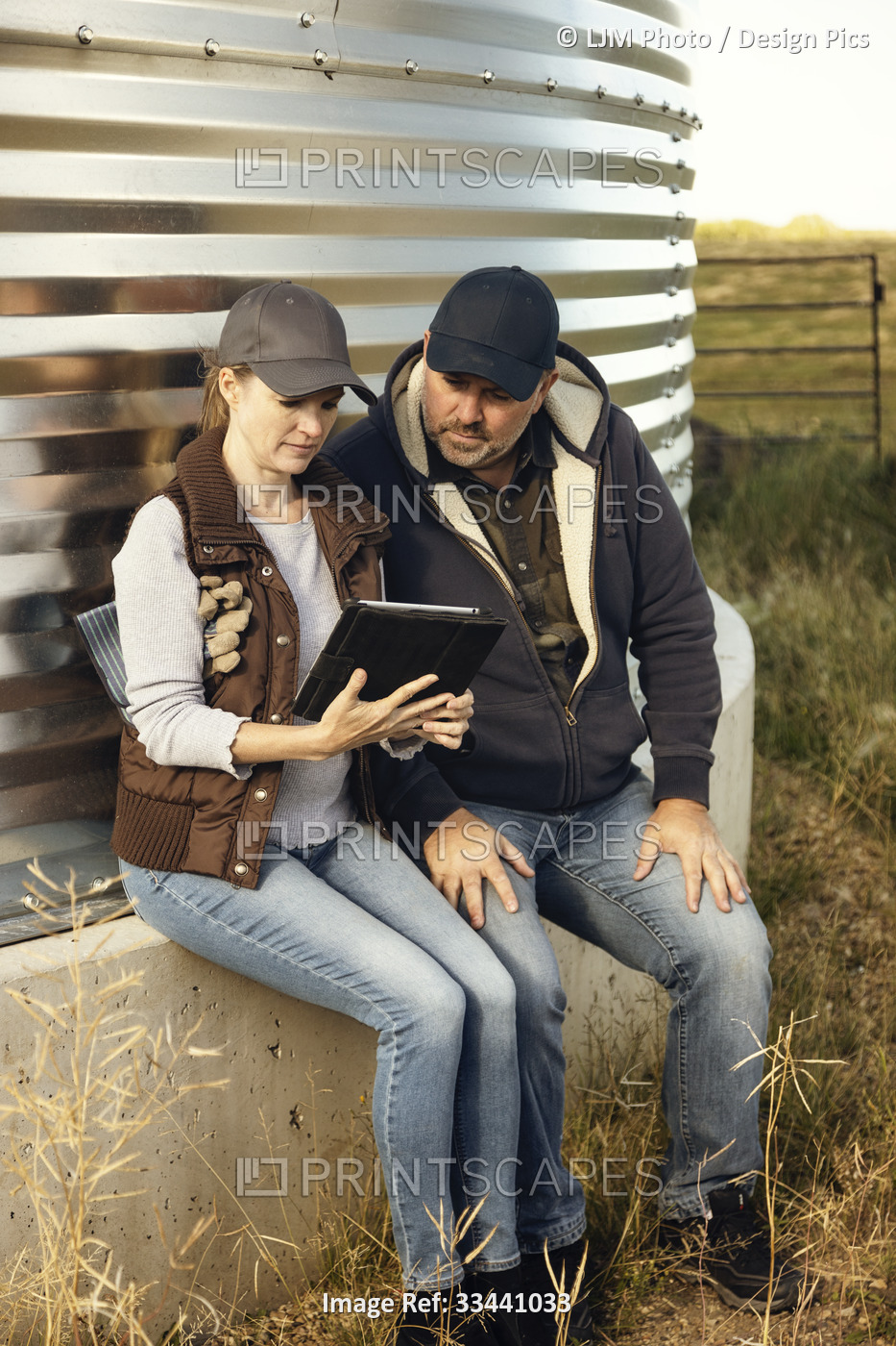 Mature couple working on their farm, sitting at on edge of a grain bin while  ...