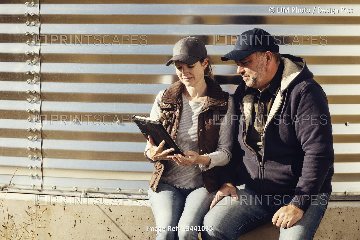 Mature couple working on their farm, sitting at on edge of a grain bin while  ...