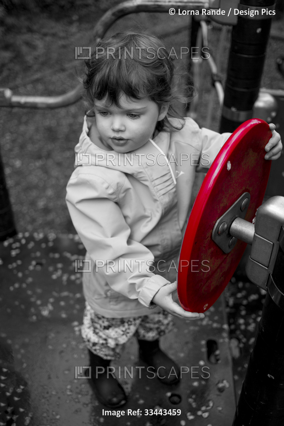 Black and white image of a preschooler girl at a playground with a vibrant red ...