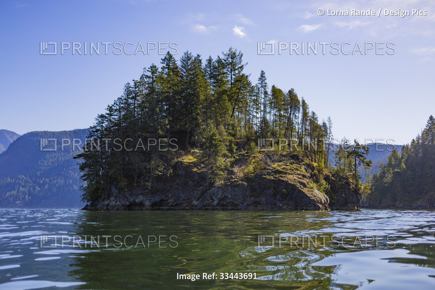 Rugged shoreline with trees on a landform reflected in tranquil water, viewed ...