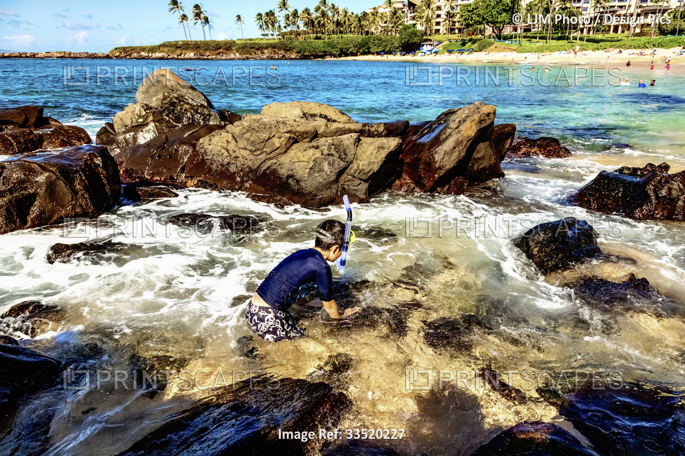 A young boy with snorkeling gear exploring the water amongst the rocks at the ...