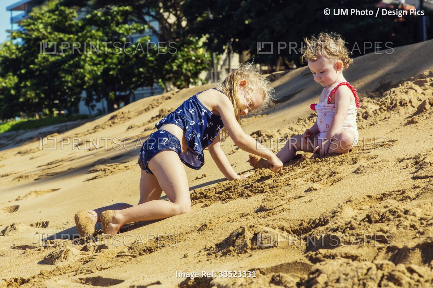 Two young girls on Ka'anapali Beach playing in the sand together; Ka'anapali, ...