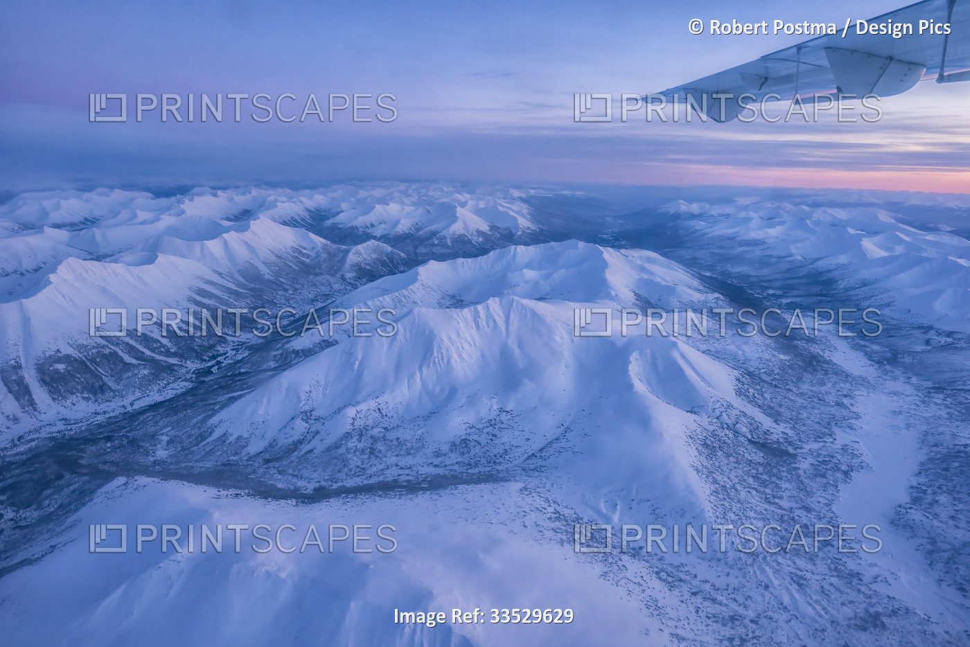 Aerial view of the Yukon during the winter with a plane wing and a pink sunrise ...