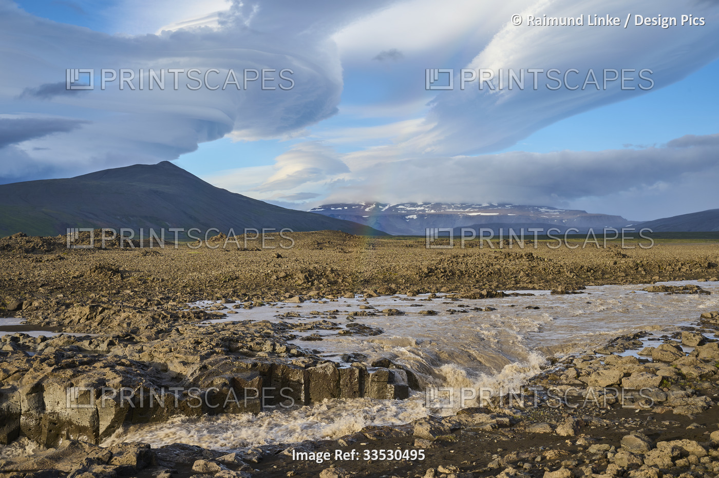Glacial river flowing through the basalt landscape with a dramatic cloudy sky ...