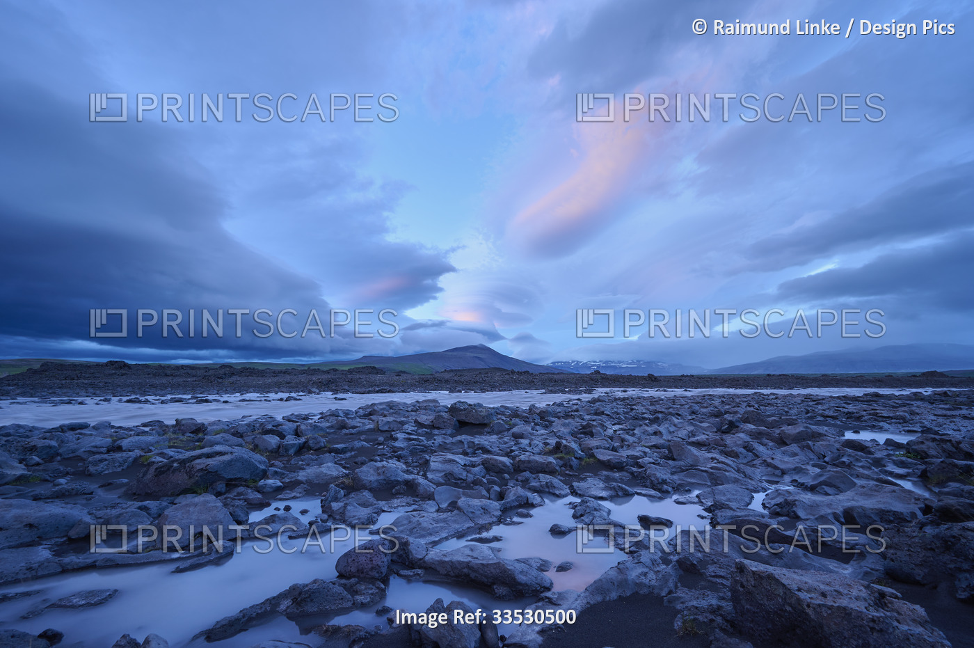 Glacial river flowing through the basalt landscape with a dramatic cloudy sky ...