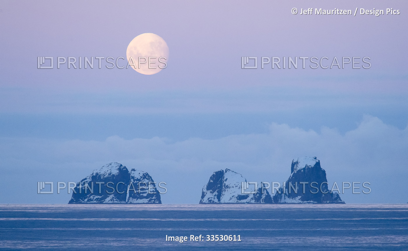 Full moon sets over two mountainous islands in the Gerlache Strait off the ...