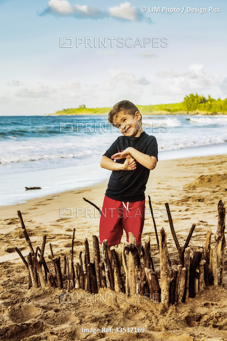A young boy stands on the beach and proudly displays his creation in the sand ...