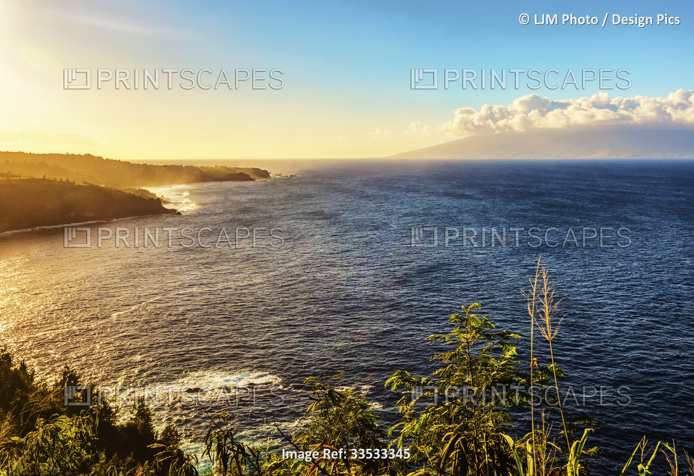 The rugged coastline of North Maui covered in lush, green foliage and the sun ...